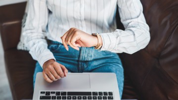 Frau mit Laptop schaut auf die Uhr