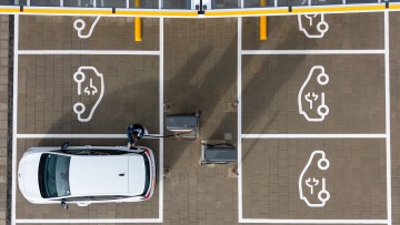 Sachsen, Klipphausen: Ein Mann steht in einem Ladepark der EnBW Energie Baden-Württemberg AG und steckt ein Ladekabel in den Tankstutzen eines Elektroautos (Aufnahme mit einer Drohne).
