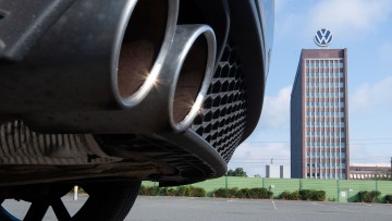 Auspuffrohre eines Volkswagen, fotografiert mit dem Markenhochhaus am VW-Werk Wolfsburg im Hintergrund. 