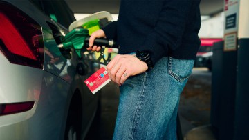 Eine Person tankt das Auto mit der Bankkarte in der Hand