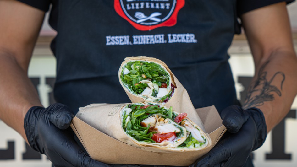 Eine Person mit schwarzen Handschuhen hält Wraps in die Kamera